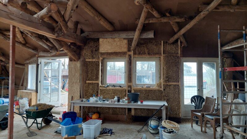 Reciprocale dakconstructie van boomstammen met strobalen en leemstuc in organische woning