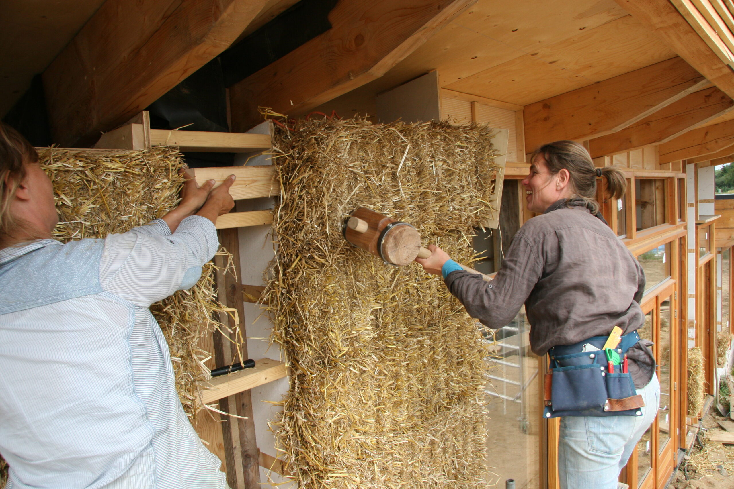 Twee mensen bevestigen een strobaal in een houten constructie — bouwen met stro