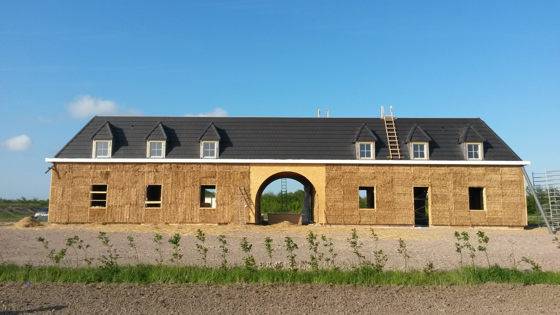 Bouwfoto — lange strogevel met centrale boog, strobalen zichtbaar in de houten constructie
