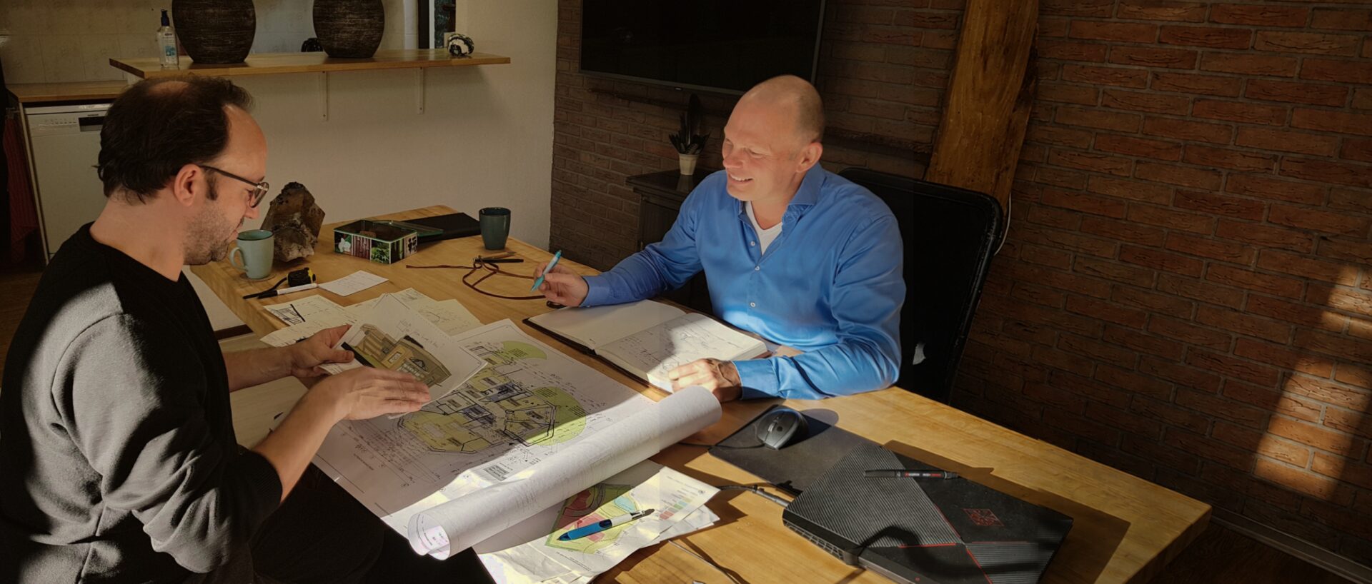 Michel Post bespreekt schetsen en bouwtekeningen met een opdrachtgever aan tafel